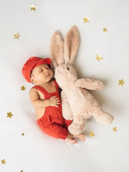 An overhead shot captures this tiny baby in red overalls, sleeping soundly next to his bunny, creating a simple and timeless newborn portrait.