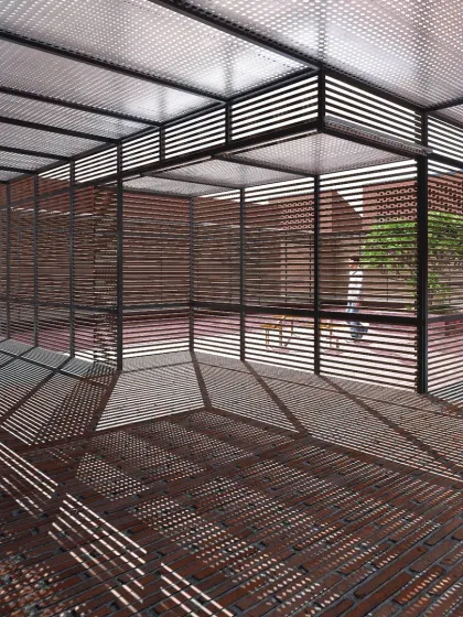 An exploration of light and shadow at Studio Tarai. The slatted steel pergola and wall screens are not just structural; they are designed to catch the sun and cast dynamic geometric patterns across the brick floor, making light a tangible material that changes throughout the day.