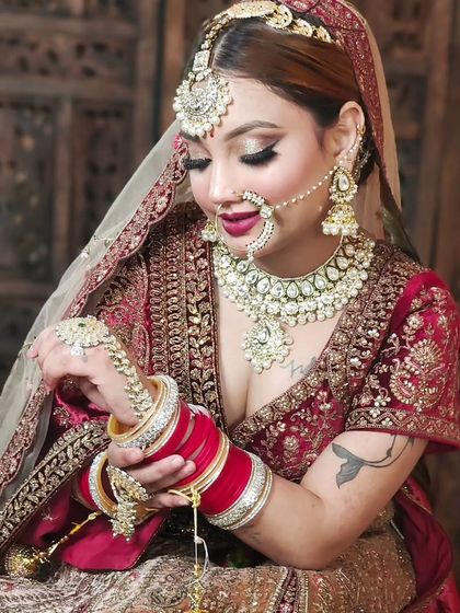 A candid shot of a bride adjusting her bangles, showcasing a complete bridal jewellery set with a choker, nath, and maang tikka. The red choora complements the traditional look perfectly.