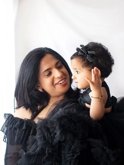 A mother sharing a smile with her little one. The simple white background and matching black dresses keep the focus on their beautiful interaction.