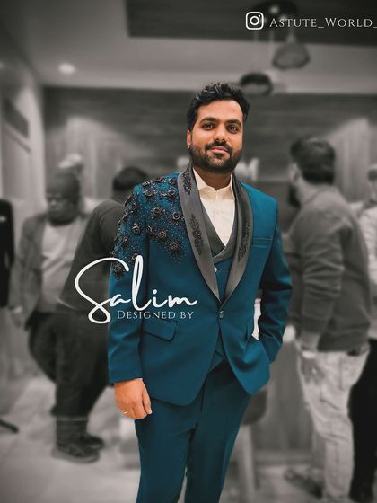 A client wearing a teal three-piece suit with black floral appliqué on the shoulder. The color combination is unique and sophisticated.