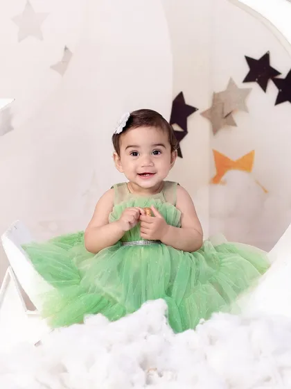 A close-up of the baby girl in the green dress, showing her happy smile and the delicate details of her outfit.