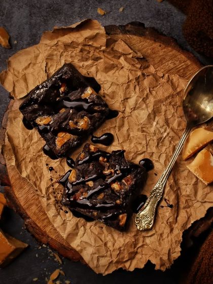 How to keep brownies fresh? Eat them all in one sitting. This dark and moody flatlay showcases decadent chocolate brownies on rustic paper, drizzled with chocolate sauce.
