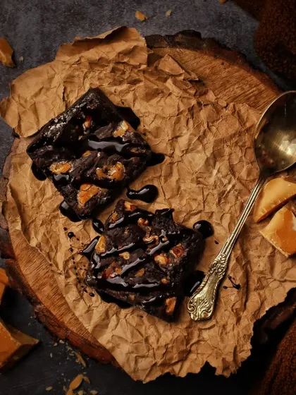 How to keep brownies fresh? Eat them all in one sitting. This dark and moody flatlay showcases decadent chocolate brownies on rustic paper, drizzled with chocolate sauce.