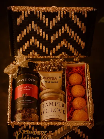 For the coffee connoisseur, this Noir & Gold festive box is pure indulgence. It features rich Davidoff coffee, almond brittle, premium cashews, and unique ladoo-shaped candles, all housed in a striking black and gold handcrafted basket for a truly luxurious feel.
