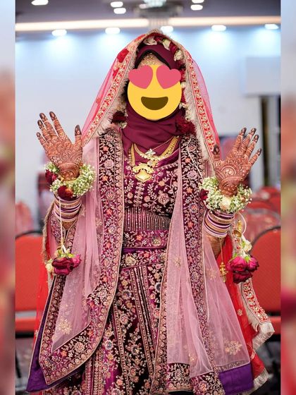 A happy bride showing off her beautiful bridal henna. The dark stain on her hands stands out beautifully against her elaborate wedding lehenga.