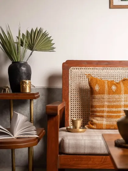 A close-up detail of the custom-designed armchair, showing the combination of teak wood, cane weaving, and brass accents that define the furniture in this home.