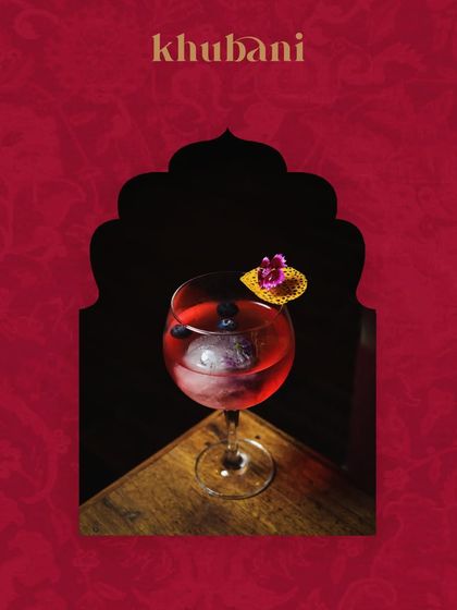 A perfect start to your week. This beautiful red cocktail, served in a balloon glass with fresh blueberries, is framed by a traditional Indian arch design.