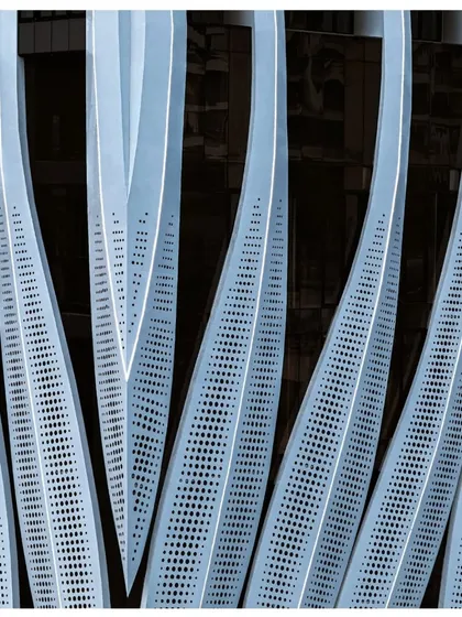 A detailed shot of the perforated facade panels, showing the gradient of perforations designed to control sunlight and create a visually interesting texture.