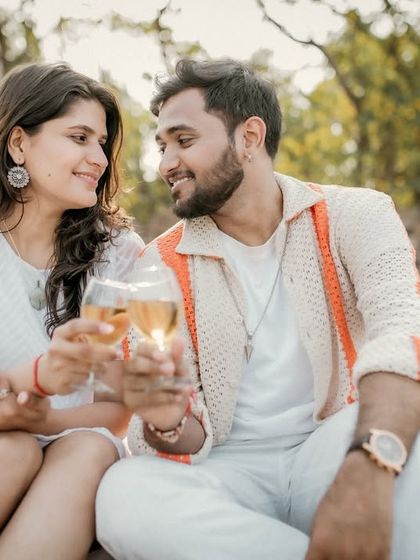 A toast to their future together. The couple clinks glasses during their romantic beach picnic, smiling at each other in a moment of shared happiness.