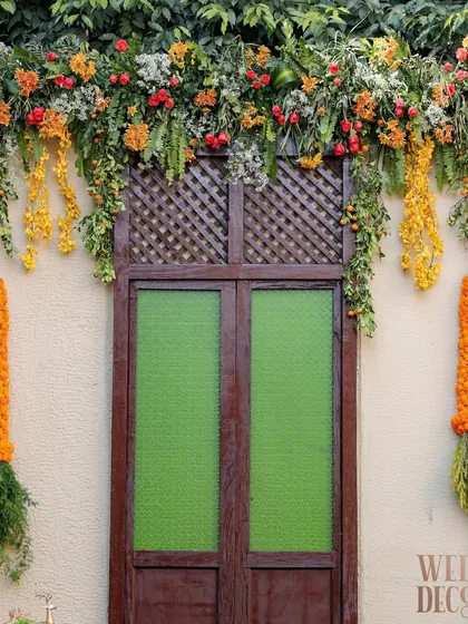 A close-up of the heritage-style door and window backdrop, adorned with fresh marigold garlands and cascading florals. This element was key to creating the 'Old Delhi' architectural feel.