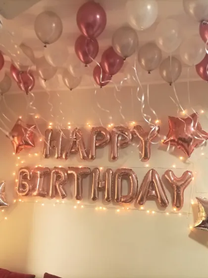 A classic and simple room decoration for a birthday surprise. Rose gold "Happy Birthday" foil letters, star-shaped foils, and balloons floating on the ceiling create a festive and celebratory feel.