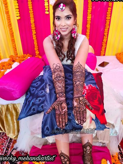 A happy bride posing for a photo during her mehndi ceremony, with her full hand and leg designs on display.