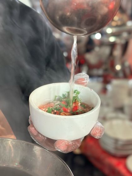 A chef pours hot, clear broth into a bowl of fresh Thai ingredients. This is the final step in creating a flavourful soup, releasing all the aromas of the herbs and spices.