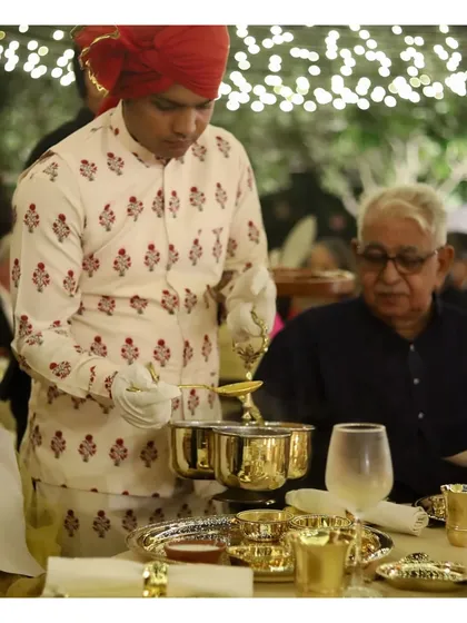 A guest is served at a traditional Indian feast, featuring ornate brass serving dishes. Our staff, dressed in elegant ethnic attire, adds to the authenticity and grandeur of the cultural dining experience we curate.