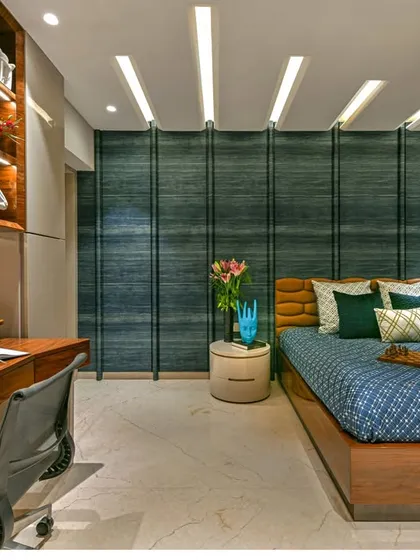 This bedroom combines a study area with a restful sleeping space. The deep teal fluted wall serves as a dramatic backdrop for the bed, while the wooden desk and light-colored cabinetry provide a functional workspace.