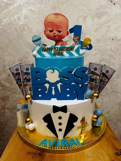 A two-tier Boss Baby cake for a first birthday, complete with a tuxedo design, edible money, and a baby bottle.