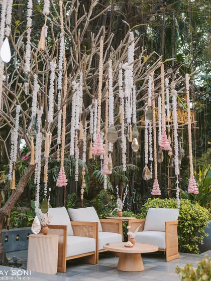 A serene lounge spot under a tree adorned with hanging floral tassels. The modern, light-wood furniture creates a clean and calming space for guests.