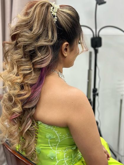 A high ponytail with voluminous curls, featuring blonde highlights and a pop of purple for a fun and trendy party look.