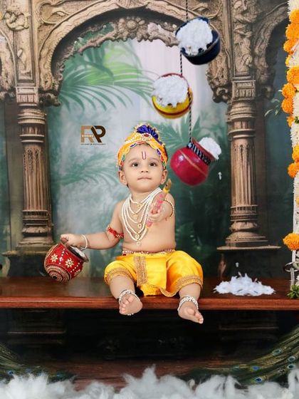 A beautiful portrait of a baby as Little Krishna, sitting on an ornate swing decorated with marigolds and peacocks. This elaborate setup creates a majestic and timeless image.