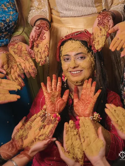 A fun and messy Haldi moment, with the bride surrounded by hands applying turmeric paste.