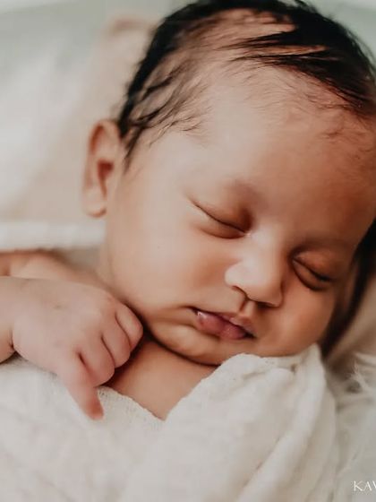 A close-up portrait focusing on the serene face of a sleeping newborn. The soft, natural lighting highlights the baby's delicate features, from their eyelashes to their tiny lips.