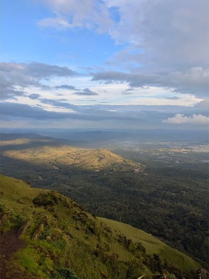 Sunlight breaking through the clouds to illuminate a patch of green forest in the Chikmagalur hills.