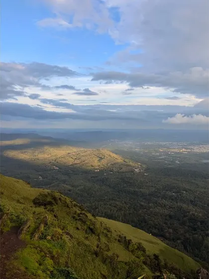 A breathtaking view from a Chikmagalur peak, with sunlight breaking through the clouds to illuminate the forest below.