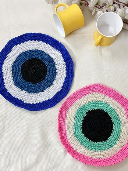 My evil eye crochet doilies are available in different color schemes, like the classic blue and a unique pastel pink and green version. They can be used as large coasters or small tablemats.