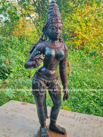 The wax model of Sivagami (Goddess Parvati) standing in a classic Chola style. The outdoor setting highlights the smooth finish and graceful posture of the wax figure before it is prepared for casting.