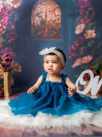 A dreamy first birthday portrait. This little girl in her beautiful blue dress looks like she's in a secret garden, creating a magical memory of turning one.
