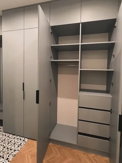 This is a great example of our functional and stylish hinged wardrobes. We designed this floor-to-ceiling unit in a modern grey Fenix finish, featuring a mix of hanging space, shelves, and soft-close drawers. The integrated entryway bench with a mirror and coat hooks makes the entire space more practical.