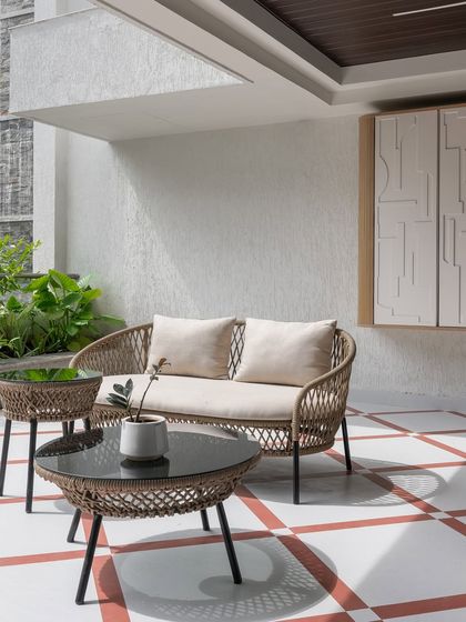 An outdoor seating area with modern woven furniture and a unique tiled floor in a terracotta and white pattern. A sculptural wall panel adds an artistic touch to this minimalist patio space.
