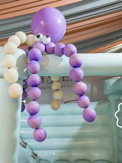 A whimsical octopus made of balloons hangs over the bouncy castle, watching over the fun.