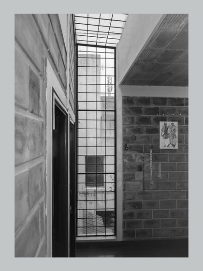 A tall, narrow window and an overhead skylight work together to draw light deep into the home. This black and white shot emphasizes the textural contrast between the smooth glass and the rough surface of the exposed brick walls.