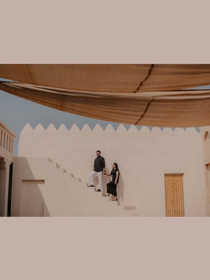 A wide, cinematic shot of the couple on a stark white staircase against a desert-hued wall, showcasing a dramatic destination.