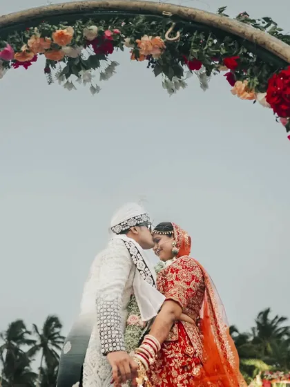 An intimate kiss under the floral arch of the beachside mandap, a perfect romantic moment.