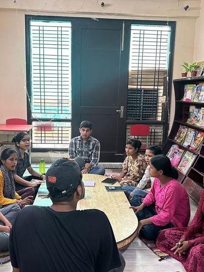 Kalakaar fellows lead a session at a community center, sitting with students around a table. This informal setting encourages open conversation and collaborative learning.