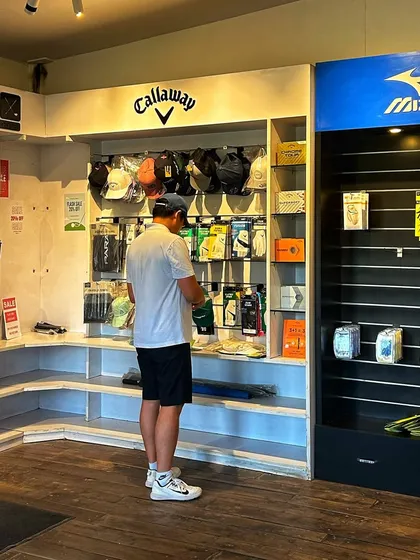 Our Pro Shop is your headquarters for the grind. A customer browses our wall of premium golf gloves and caps from brands like Callaway and Mizuno, fully stocked for your needs.