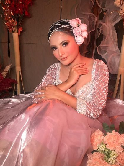 A serene portrait in a dreamy setting. The soft lighting complements the shimmering pink outfit and the radiant makeup.