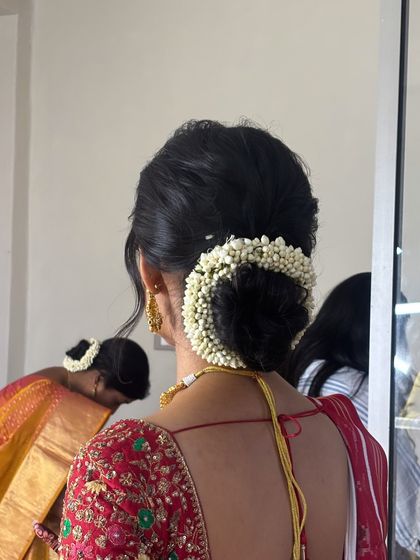 The back view of a traditional bridal hairstyle, showing a neat low bun fully encircled by a fragrant jasmine gajra. This is a timeless choice for wedding ceremonies.