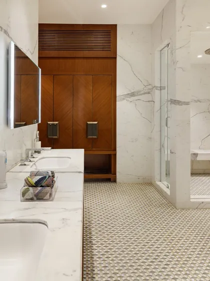 This bathroom is a private retreat within the home. Sleek marble finishes are paired with the warmth of wooden accents, while patterned flooring adds texture and depth. Every element is curated for comfort and refinement.