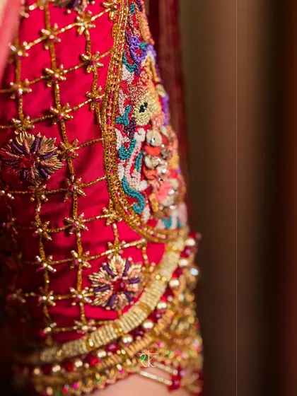 An extreme close-up showcasing the fine craftsmanship of a hand-embroidered sleeve. Notice the texture of the zardosi, the shimmer of the beads, and the precision of each stitch that forms the elaborate floral and peacock patterns.
