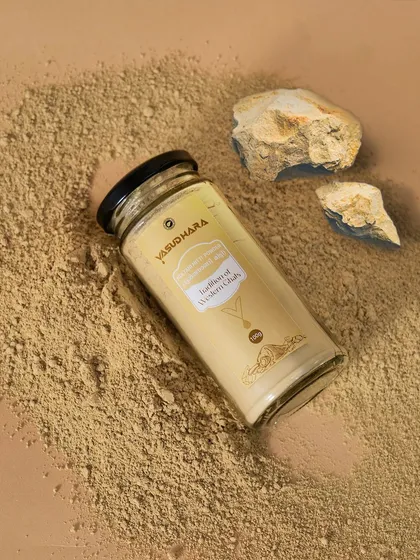 An overhead shot of a Vasudhara face pack jar with powder and stones. This flat-lay style is popular for social media and gives a clear view of the product and its texture.