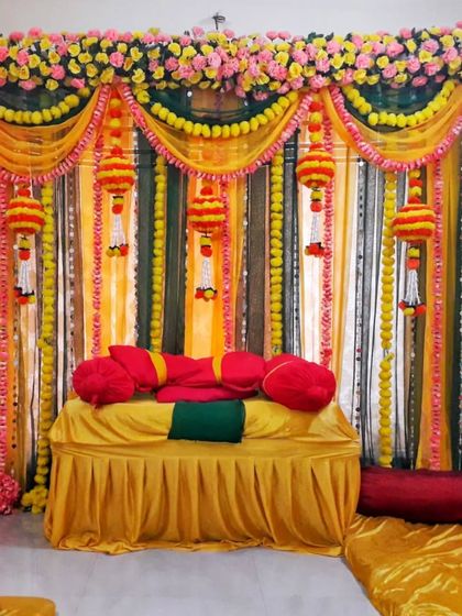 A complete Haldi decoration for a home, with a fabric backdrop, marigold hangings, and comfortable floor seating with bolsters.
