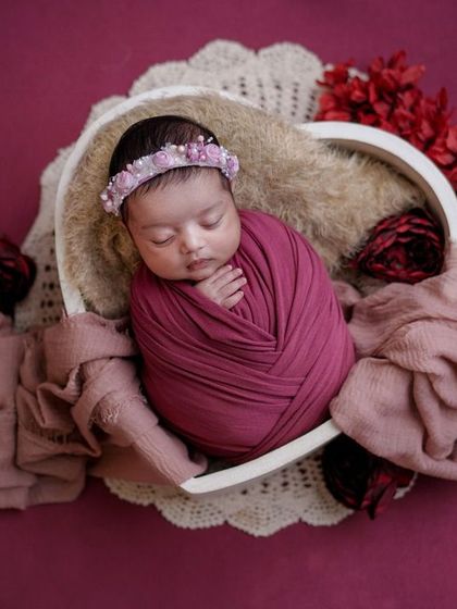 A heart full of flowers. This baby is nestled in a heart-shaped bowl, surrounded by rich magenta tones and delicate red roses.