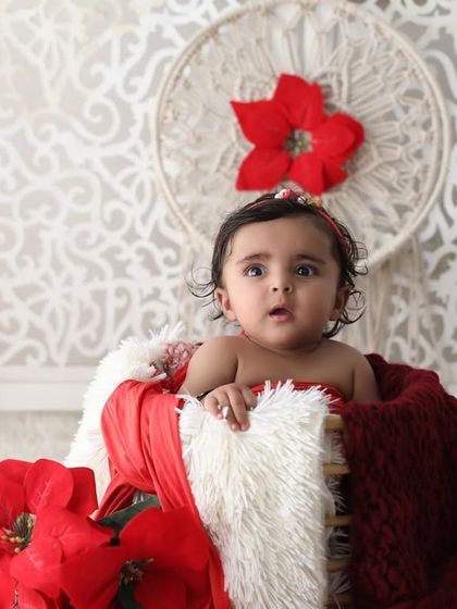 This five-month-old baby is sitting up in a basket, looking right at the camera. The festive red and white setup adds a touch of holiday cheer to this adorable milestone portrait.