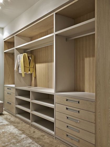 This open-concept walk-in closet uses a light wood finish to create a bright and airy feel. The design includes a mix of drawers with premium metal handles, open shelves, and dedicated sections for long and short garments.