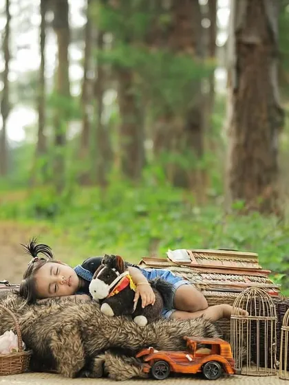 An artistic outdoor shot of a one-year-old sleeping peacefully on a bed of vintage props in a forest setting.