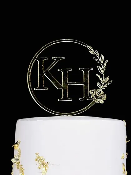 A close-up of a custom acrylic monogram topper with a delicate floral design, adding a personal and elegant touch to a royal engagement cake.